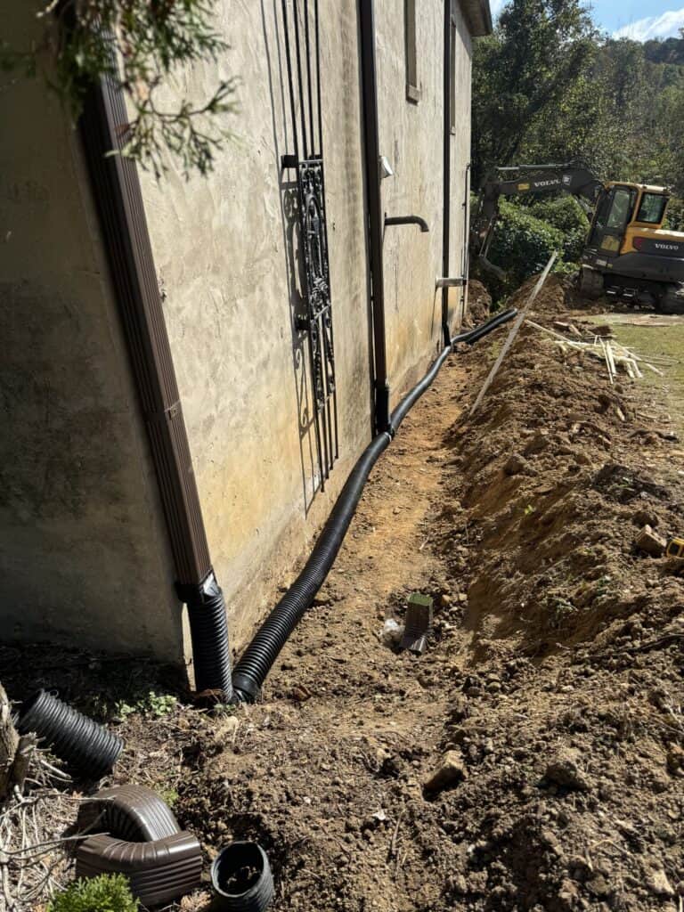 Excavation and drainage pipe installation beside a home.